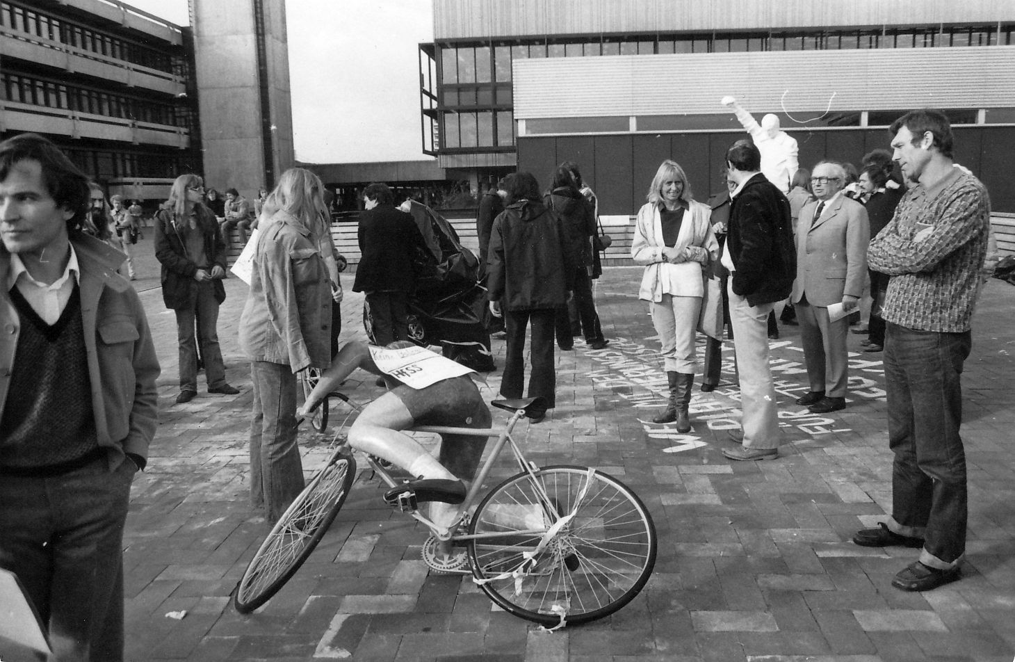 Schwarz-Weiß-Aufnahme einer Protestaktion. Im Zentrum eine Radrennfahrer-Skulptur auf dem Boulevard der Universität. Dazwischen stehen Protestierende. Auf dem Boden ist ein Protestaufruf gemalt.