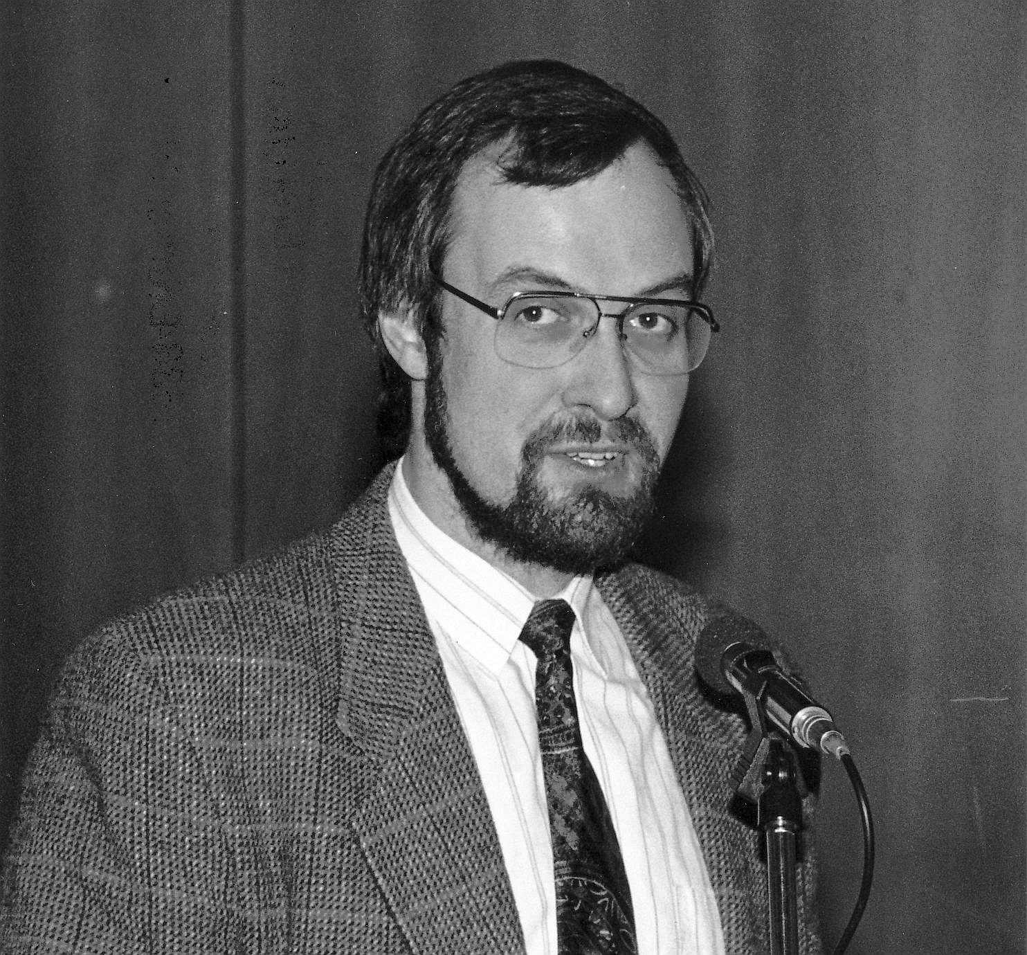 Jürgen Gutowski bei seiner Wahl zum Konrektor 1995. Er steht am Mikrofon, anscheinend zum Publikum sprechend. Er trägt ein kariertes Jackett und eine gemusterte Krawatte.