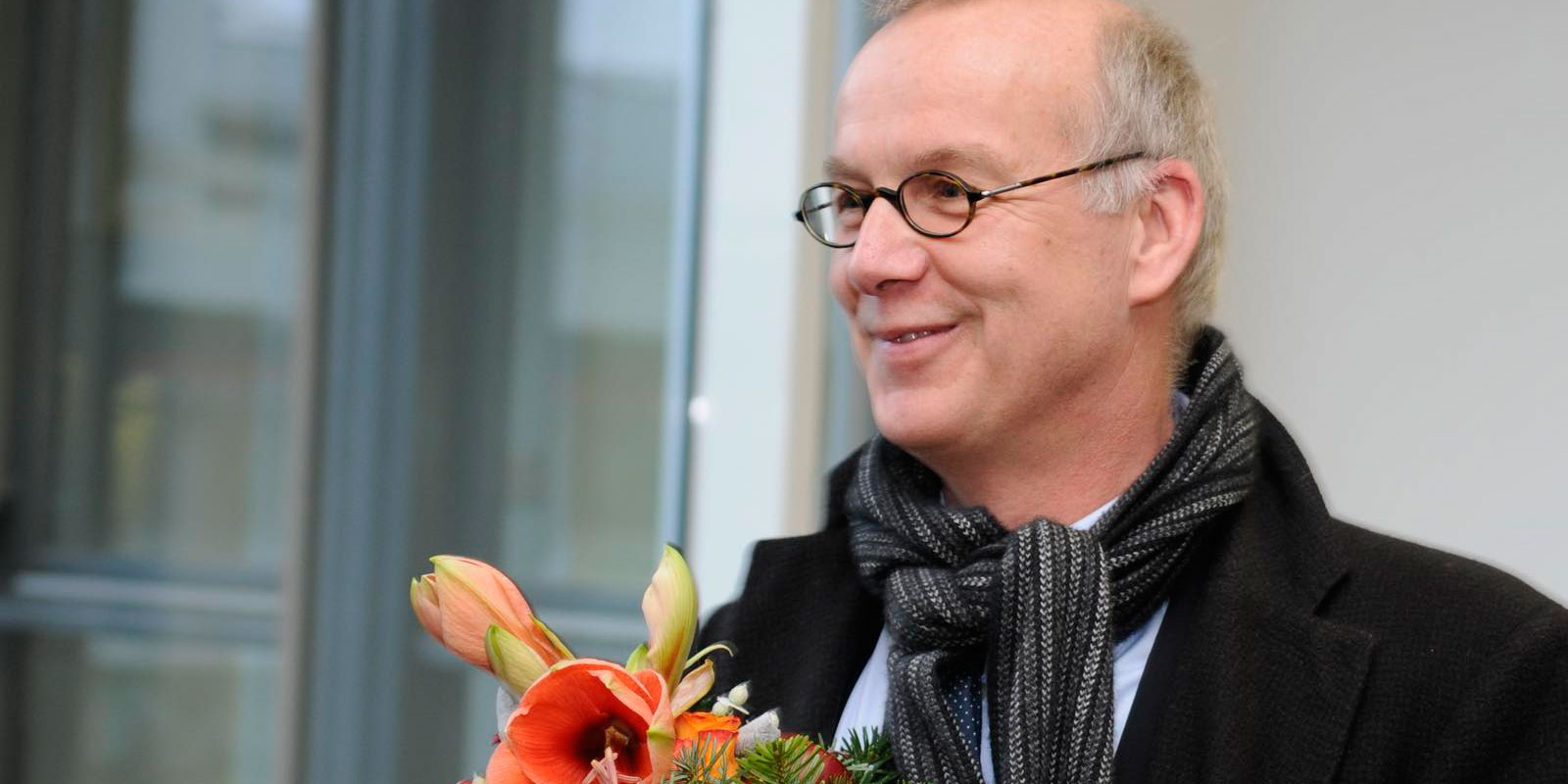 Man sieht Bernd Scholz-Reiter von der Seite wie er lächelt und einen Blumenstrauß in den Händen hält.