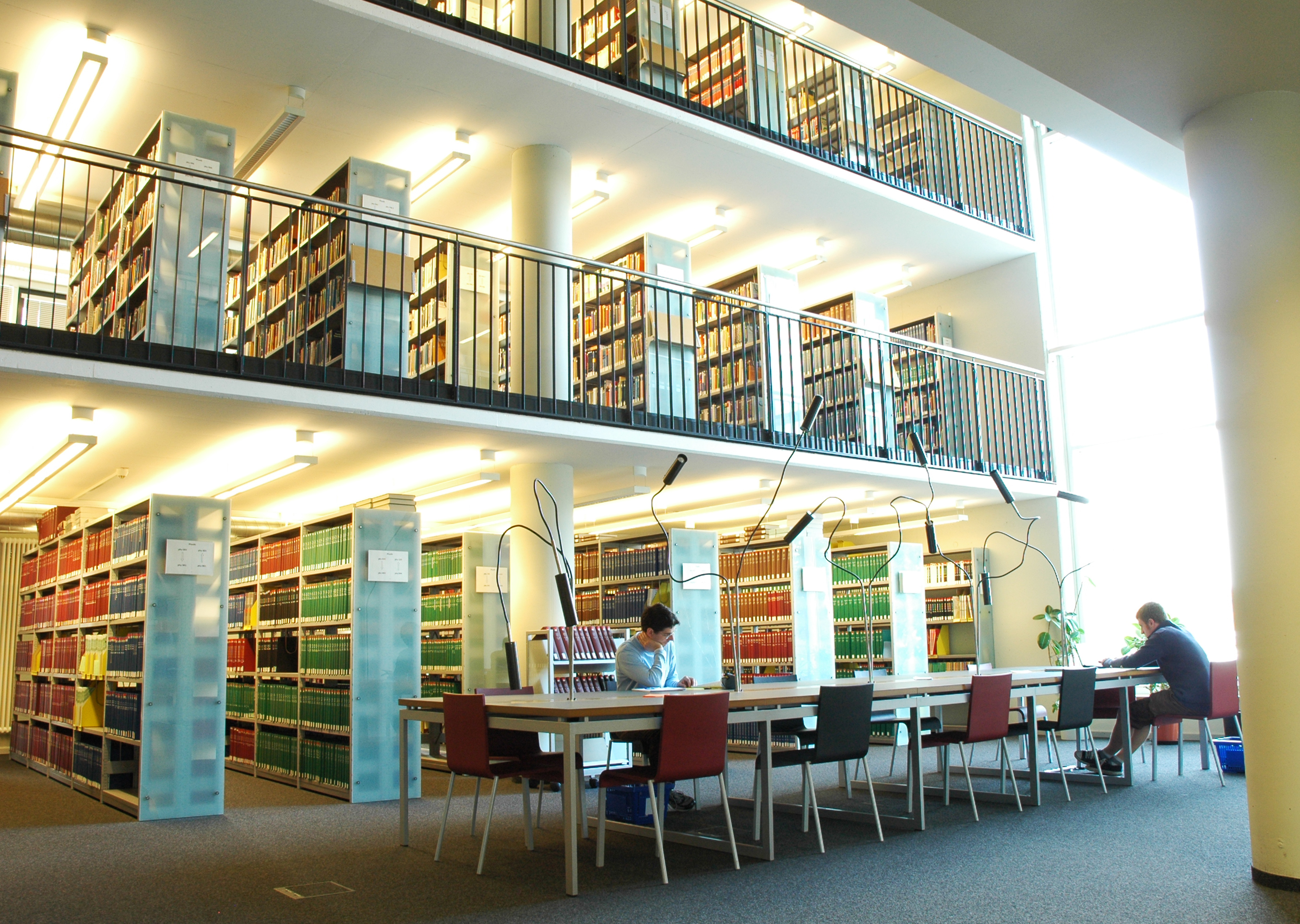 Eine Bibliothek, die über drei Etagen verfügt und auf denen sich Regale mit Büchern und auf der untersten Etage ein Arbeitstisch befinden.