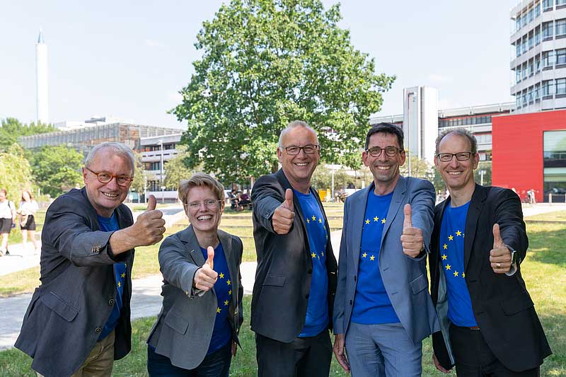 Mitglieder des Rektorats stehen vor dem Zentralbereich der Uni Bremen und zeigen mit freudiger Geste „Daumen hoch“.